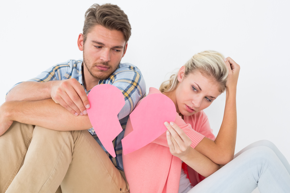 Young couple holding two halves of broken heart over white background